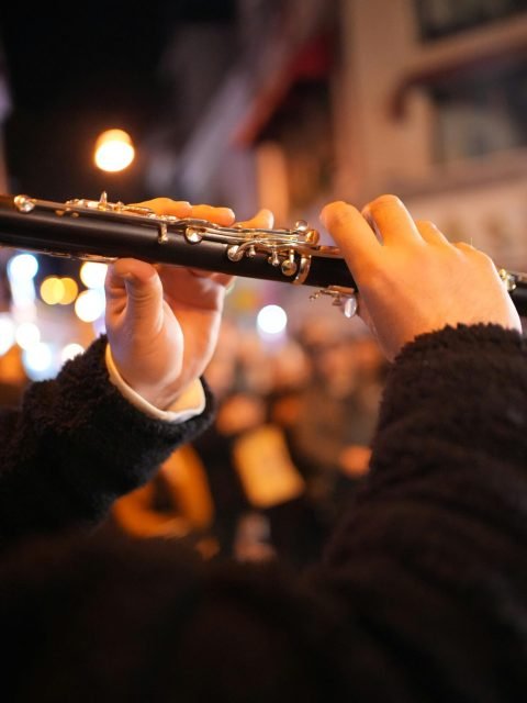 A street musician plays the flute in a vibrant city night scene with blurred lights.